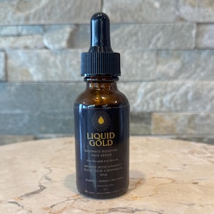 May include: A brown glass bottle of Liquid Gold Radiance-Boosting Face Serum with a black dropper. The label includes the product name and ingredients, such as Vitamin C and botanical oils.