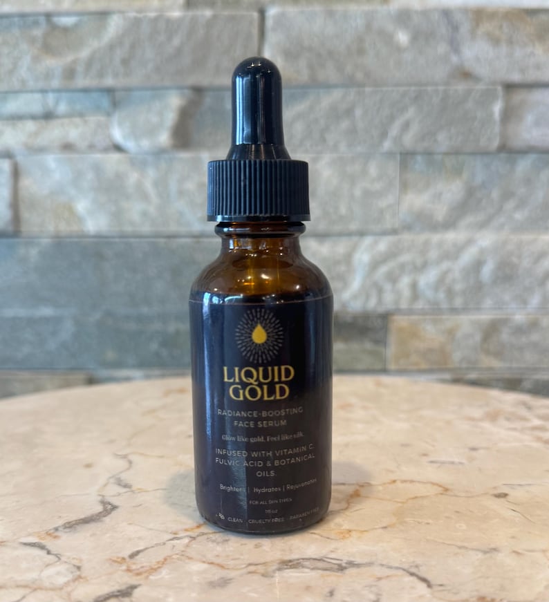 May include: A brown glass bottle of Liquid Gold Radiance-Boosting Face Serum with a black dropper. The label includes the product name and ingredients, such as Vitamin C and botanical oils.