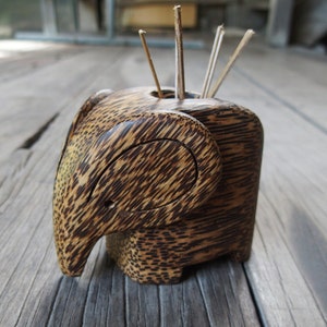 May include: A wooden elephant toothpick holder with a brown and tan striped pattern. The holder has a small opening on the top for toothpicks.