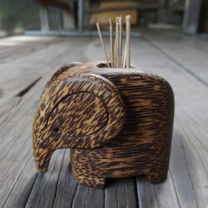 May include: A wooden elephant toothpick holder with a dark brown finish. The holder has a slot for toothpicks and is carved in the shape of an elephant.
