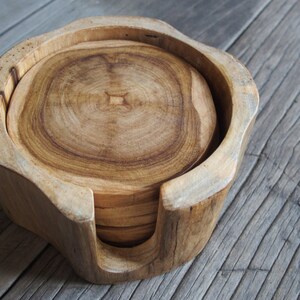 May include: A set of wooden coasters in a holder made from a tree trunk. The coasters are round and have a natural wood finish. The holder is made from a piece of wood that has been carved to create a unique shape.