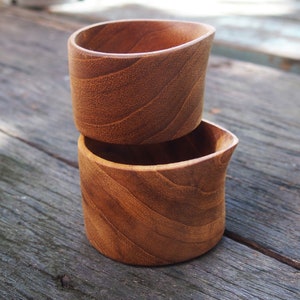 May include: Two wooden bowls stacked on top of each other. The bowls are made of a light brown wood with a natural grain pattern. The bowls are round and have a slightly curved shape.