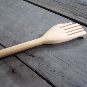 May include: A wooden back scratcher with a hand-shaped design. The scratcher has five raised ridges on the hand.
