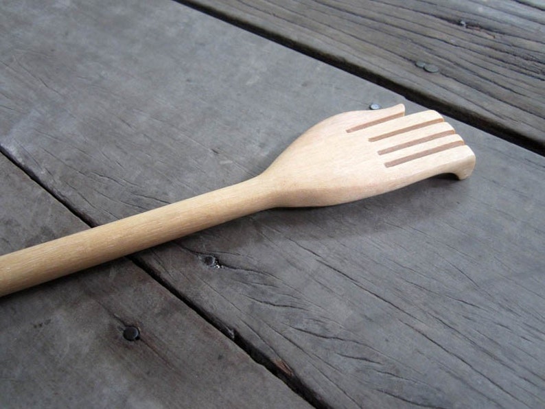 May include: A wooden back scratcher with a hand-shaped design. The scratcher has five raised ridges on the hand.