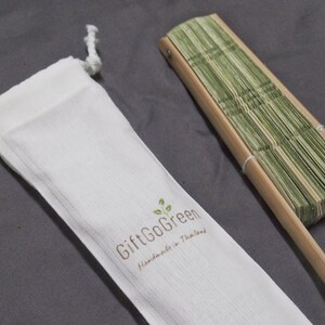 K&ouml;nnte beinhalten: Ein gr&uuml;ner Bambus-Faltf&auml;cher mit einem Holzgriff, kommt mit einem wei&szlig;en Kordelzugbeutel, auf dem "GiftGoGreen Handmade in Thailand" steht.