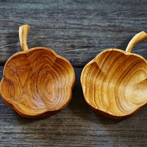 Puede incluir: Dos cuencos de madera con forma de hoja y un asa. Los cuencos están hechos de madera marrón claro con un patrón de veta natural.