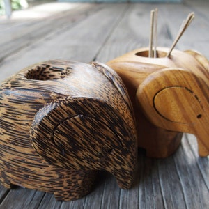 May include: Two wooden elephant figurines, one with a dark brown wood grain and the other with a light brown wood grain. The dark brown elephant has a small hole in the top of its head, while the light brown elephant has a small hole in the top of its head and a small hole in its trunk.