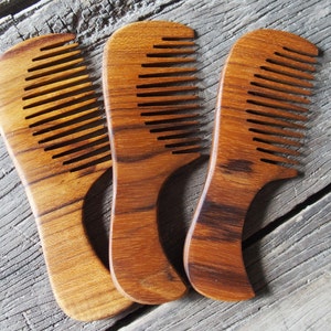 May include: Three wooden combs with a natural brown finish. The combs have a curved shape and are made of a dark wood with a grain pattern.