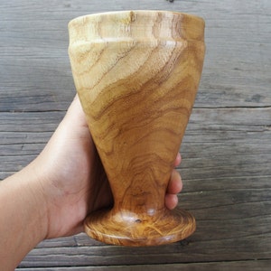 May include: A wooden goblet with a natural wood finish. The goblet has a wide base and a tall, slender body.