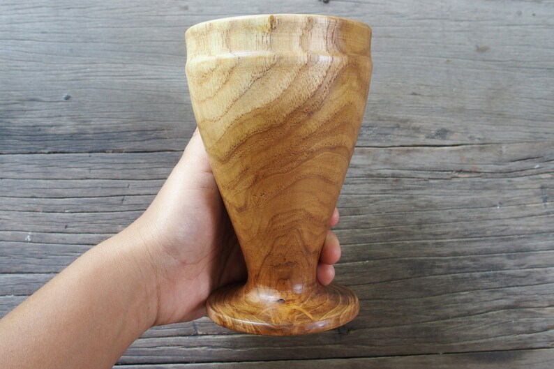 May include: A wooden goblet with a natural wood finish. The goblet has a wide base and a tall, slender body.