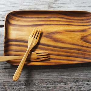 Könnte beinhalten: Zwei Holzgabeln auf einem rechteckigen Holztablett mit natürlicher Holzmaserung.