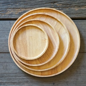 May include: Four wooden serving trays of varying sizes, nested together, with a natural wood grain finish. The trays are round and have a slightly raised edge.