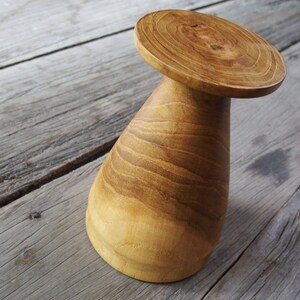 May include: A wooden pedestal with a wide, round top and a conical base. The wood has a rich, brown color and a natural grain pattern.