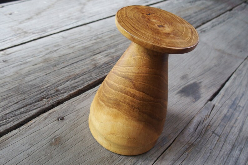 May include: A wooden pedestal with a wide, round top and a conical base. The wood has a rich, brown color and a natural grain pattern.