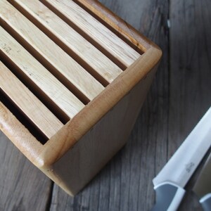 Puede incluir: Un bloque de cuchillos de madera con acabado marr&oacute;n claro, con ranuras para guardar cuchillos. Dos cuchillos de acero inoxidable con mangos grises est&aacute;n colocados cerca. Los cuchillos tienen hojas plateadas y mangos grises.