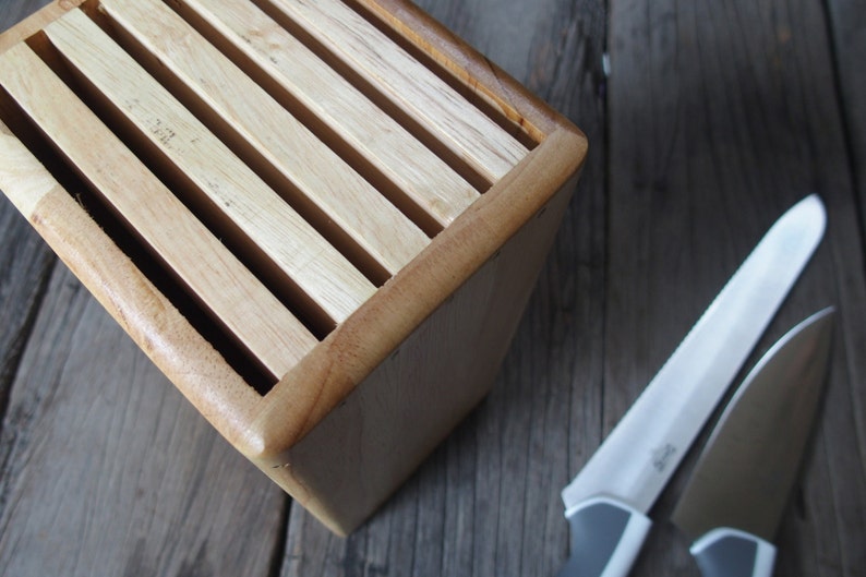 Puede incluir: Un bloque de cuchillos de madera con acabado marr&oacute;n claro, con ranuras para guardar cuchillos. Dos cuchillos de acero inoxidable con mangos grises est&aacute;n colocados cerca. Los cuchillos tienen hojas plateadas y mangos grises.
