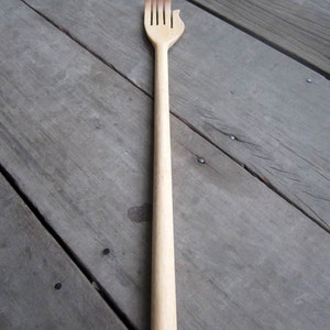 May include: A wooden back scratcher with a hand-shaped top and five prongs. The scratcher is light brown and has a smooth finish.