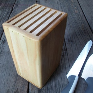 Puede incluir: Un bloque de cuchillos de madera clara con ranuras para almacenamiento. Dos cuchillos con hojas plateadas y mangos grises est&aacute;n junto al bloque. El bloque est&aacute; sobre una superficie de madera envejecida.