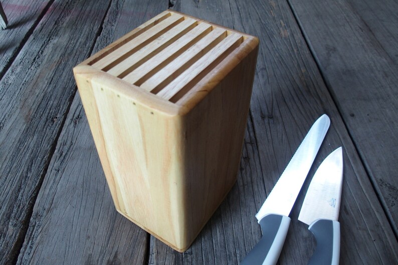 Puede incluir: Un bloque de cuchillos de madera clara con ranuras para almacenamiento. Dos cuchillos con hojas plateadas y mangos grises est&aacute;n junto al bloque. El bloque est&aacute; sobre una superficie de madera envejecida.