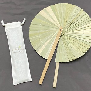 K&ouml;nnte beinhalten: Ein hellgr&uuml;ner Bambus-Handf&auml;cher mit einem Holzgriff. Der F&auml;cher ist zusammengeklappt und wird mit einem wei&szlig;en Stoffbeutel mit dem Text "GiftGoGreen Handmade in Thailand" geliefert.