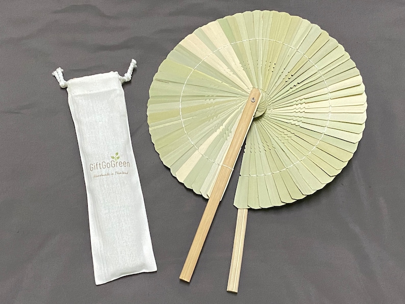 K&ouml;nnte beinhalten: Ein hellgr&uuml;ner Bambus-Handf&auml;cher mit einem Holzgriff. Der F&auml;cher ist zusammengeklappt und wird mit einem wei&szlig;en Stoffbeutel mit dem Text "GiftGoGreen Handmade in Thailand" geliefert.
