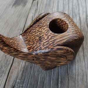 May include: A wooden elephant-shaped trinket box with a dark brown and black wood grain pattern. The box has a round opening on the top.