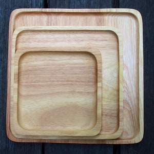 Op de afbeelding: Drie houten serveerschalen, in elkaar geschoven, met een vierkante vorm en een lichtbruine kleur. De schalen zijn gemaakt van natuurlijk hout en hebben een gladde afwerking.