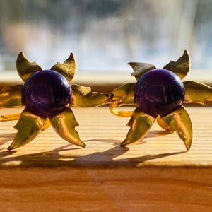 ¡Excelente conjunto de aretes vintage con estrella dorada y flor en tono morado brillante!