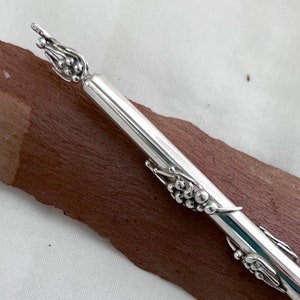 Może przedstawiać: Srebrny długopis z wzorem winorośli. Długopis jest wykonany z metalu i ma gładkie, polerowane wykończenie.