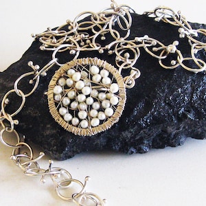 May include: A silver chain necklace with a circular pendant featuring a cluster of white pearls set in a wire mesh design.