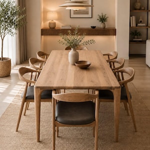 May include: A rectangular light oak dining table with eight matching wooden chairs featuring curved backrests and dark gray upholstered seats. A ceramic vase with green branches and a small wooden bowl sit in the center of the table.