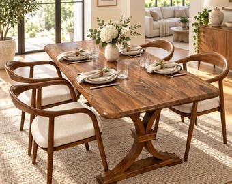 Puede incluir: Una mesa de comedor rectangular de madera con base de caballete y cuatro sillas a juego con respaldos curvos y asientos tapizados en color beige claro. La mesa está puesta con platos blancos, servilletas, vasos y un centro de flores.