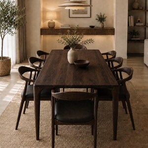 May include: A rectangular dark brown wooden dining table with eight matching chairs featuring curved backrests and black upholstered seats. The table surface is smooth and flat, supported by four sturdy legs, creating a cohesive furniture set.