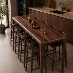 May include: A tall rectangular wooden bar table with rounded corners and six matching high stools featuring dark brown upholstered seats. The table surface displays a rich wood grain pattern and holds a glass decanter and several drinking glasses.