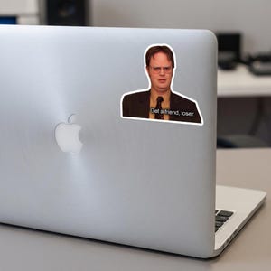 May include: A white sticker featuring a portrait of a man in a suit and glasses. The sticker has the text "Get a friend, loser."