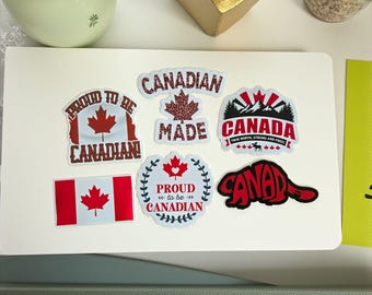 Op de afbeelding: Een verzameling stickers met een Canadees thema, met de Canadese vlag, esdoornbladeren en tekst zoals "Canadian Made" en "Proud to be Canadian". De stickers zijn in rood, wit en zwart.