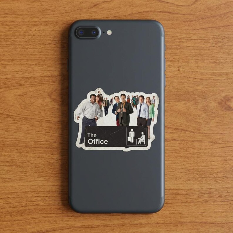 May include: A sticker featuring a group of people, with the text "The Office" and a small graphic of a person with a suitcase and a person sitting in a chair. The sticker is on a dark gray phone.