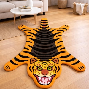 Könnte beinhalten: Ein orange-schwarzer Teppich in Tigerform mit detailliertem Gesicht und Streifenmuster. Der Teppich besteht aus weichem Material und ist als Tigerfell gestaltet. Er liegt auf einem Holzboden.