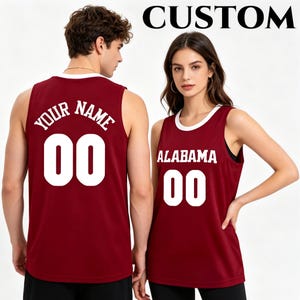 Op de afbeelding: Twee mouwloze bordeauxrode shirts met witte randen bij de hals en armsgaten. Het linker shirt heeft de tekst YOUR NAME en het nummer 00 in het wit. Het rechter shirt heeft de tekst ALABAMA en het nummer 00 in het wit. CUSTOM staat bovenaan.