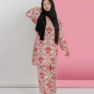 May include: A matching two-piece outfit featuring a long-sleeved top and pants. The ensemble is adorned with a repeating burgundy and cream-colored ornate pattern. The person in the image is wearing a black hijab and gold sandals.