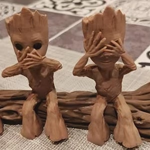May include: A set of three brown figurines, each in a different pose representing "See no evil, hear no evil, speak no evil". The figures, resembling trees, are seated on a log, with each covering their eyes, mouth, or ears.