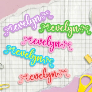May include: A collection of colorful name stickers, each featuring the name "Evelyn" in a cursive font with a bow accent. The stickers are in various colors, including purple, green, pink, blue, and coral, set against a grid background.