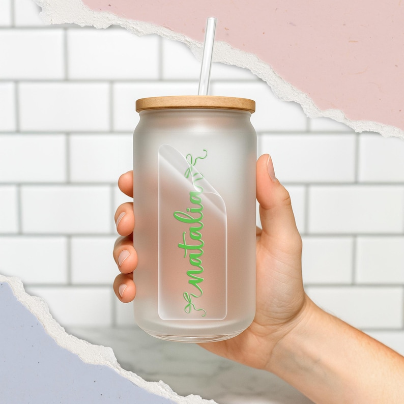 K&ouml;nnte beinhalten: Ein Glasbecher aus Milchglas mit einem Holzdeckel und einem wei&szlig;en Strohhalm. Der Becher hat den gr&uuml;nen Namen "natalia" in Schreibschrift auf einem transparenten Aufkleber. Der Becher wird von einer Hand gehalten.