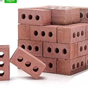 Puede incluir: Un conjunto de ladrillos de arcilla roja, cada uno con tres agujeros circulares. Dos ladrillos están separados de la pila principal. Los ladrillos son de color marrón rojizo y probablemente se utilizan para la construcción.