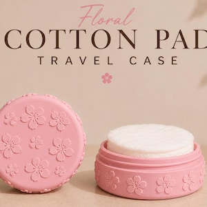 Op de afbeelding: Een roze reisetui voor wattenschijfjes met bloemmotieven. De ronde behuizing is versierd met reliëf bloemmotieven. De behuizing is open en onthult witte wattenschijfjes binnenin. De tekst "Floral Cotton Pad Travel Case" staat bovenaan.