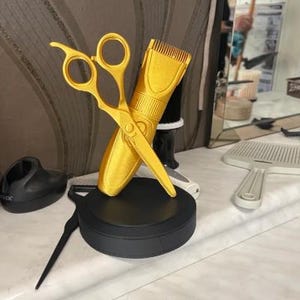 Puede incluir: Unas tijeras y una cortadora de pelo doradas se cruzan sobre una base negra. Las tijeras están abiertas y la cortadora tiene una cuchilla detallada. Otras herramientas de peluquería son visibles en el fondo.