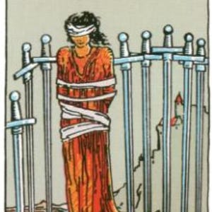 May include: Tarot card illustration featuring a figure bound and blindfolded, standing before eight swords. The figure wears an orange robe and is wrapped in white bandages. The card is labeled "VIII" at the top, with a castle in the background.