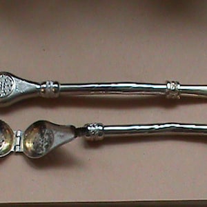 Può includere: Due infusori per tè in argento, uno con un bulbo rotondo e l'altro con due bulbi rotondi che si aprono e si chiudono. Entrambi gli infusori hanno un manico lungo e sottile.