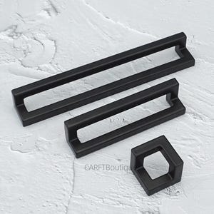 May include: A set of matte black cabinet handles and a knob. The set includes two rectangular handles of different sizes and a square knob. The hardware has a modern design and is displayed on a textured white surface.