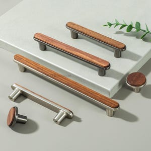 May include: A collection of modern cabinet hardware featuring wooden and metal finishes. The image showcases several cabinet pulls and knobs with a combination of wood grain and brushed metal. The hardware is designed for drawers and cabinets.